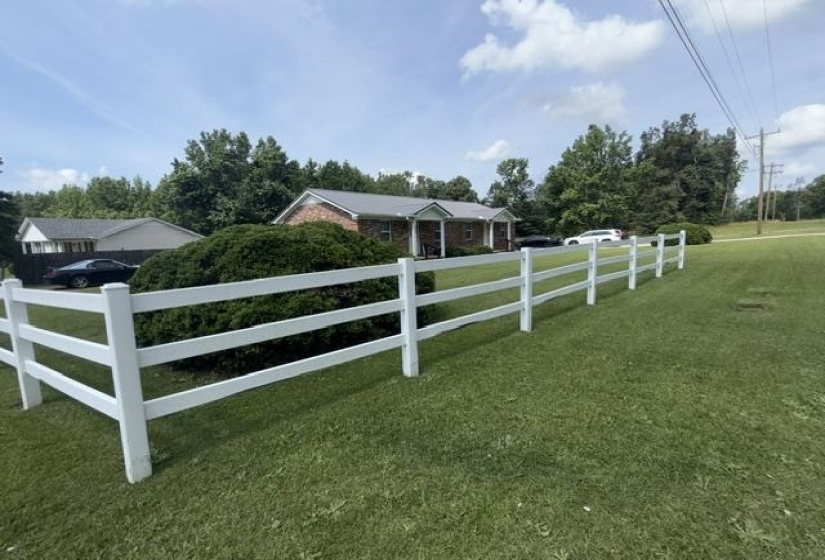 White three-rail fence framing a manicured lawn with mature landscaping