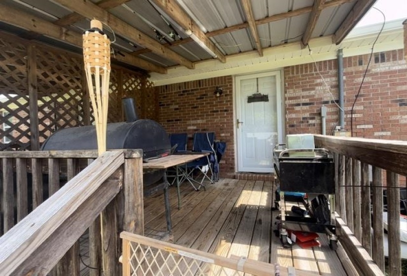 Covered deck with wood-finish flooring, brick exterior, and white entry door