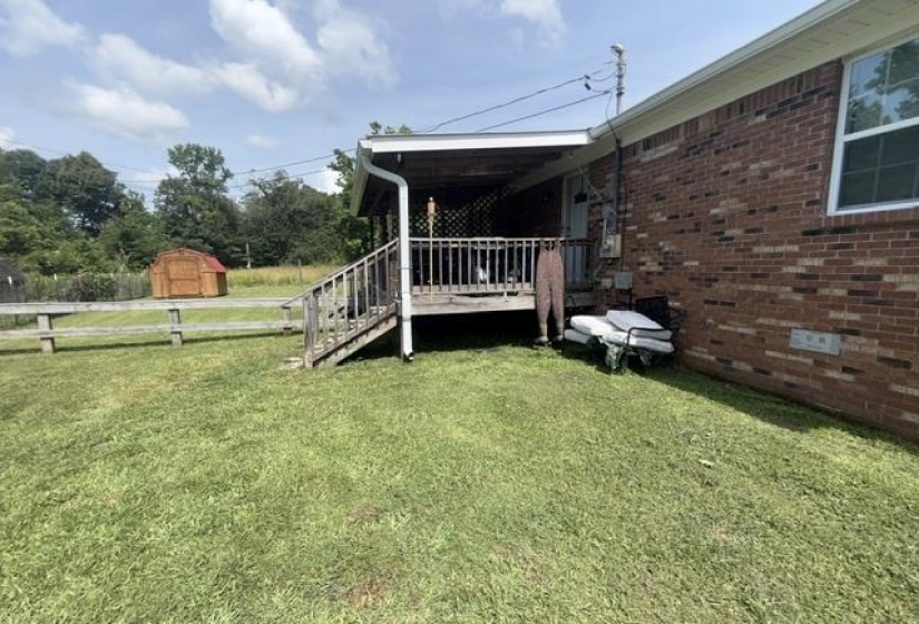 Brick exterior with a covered patio, wooden stairs, and a wooden fence