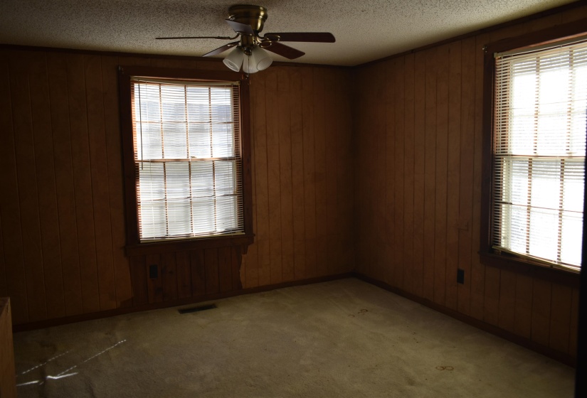 Empty room with a textured ceiling, wood walls, light colored carpet, and a ceiling fan