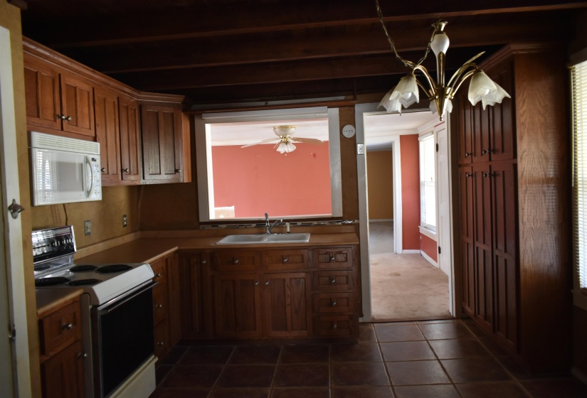 Kitchen with electric stove, white microwave, dark tile patterned flooring, pendant lighting, and a chandelier