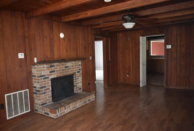 Unfurnished living room with a fireplace, dark wood finished floors, wood walls, beam ceiling, and ceiling fan