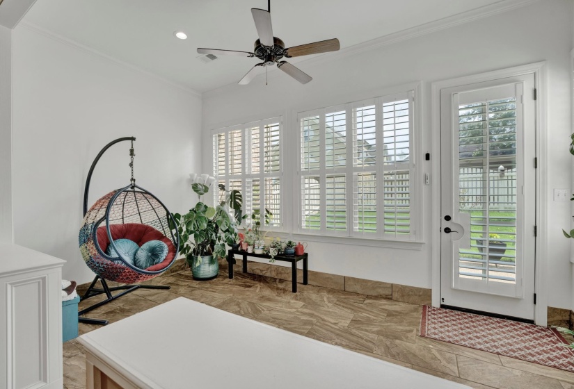 Bright interior space featuring a ceiling fan, white crown molding, large window with plantation shutters, a glass-paneled door, and wood-finish flooring