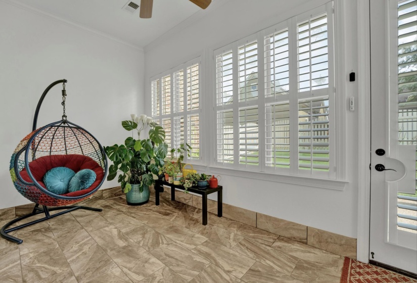 Bright sunroom featuring tile flooring, multiple windows with white plantation shutters, a glass-paneled exterior door, and a ceiling fan