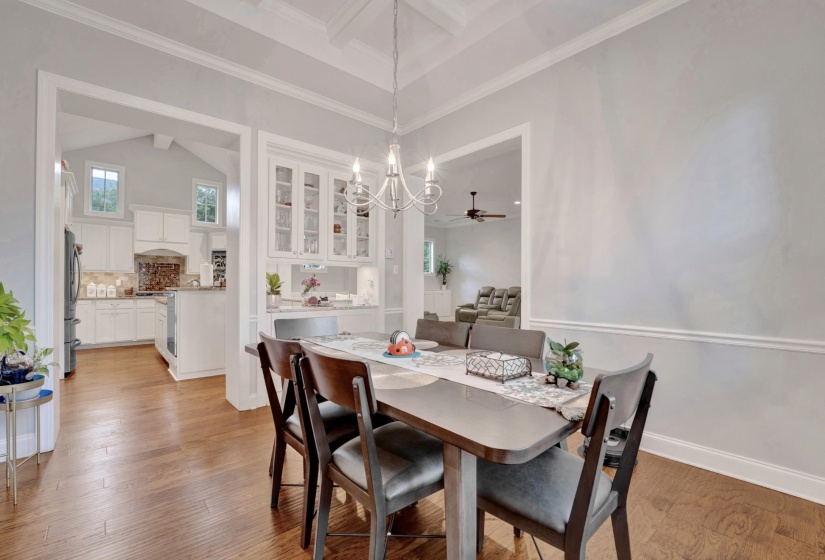 Dining area with wood-finish flooring, white tray ceiling, and a chandelier, featuring a built-in display cabinet with glass doors and under-cabinet lighting