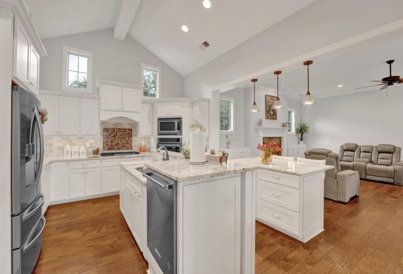 Open-concept kitchen featuring white cabinetry, light-toned granite countertops, and wood-finish flooring