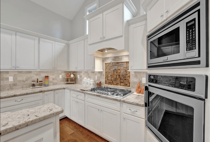 Gourmet kitchen featuring white cabinetry, light-toned countertops, a multi-tone tile backsplash, a built-in microwave, and a wall oven