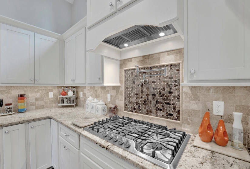 Gourmet kitchen featuring a stainless steel gas range, pot filler, custom range hood, mosaic tile backsplash, and granite countertops
