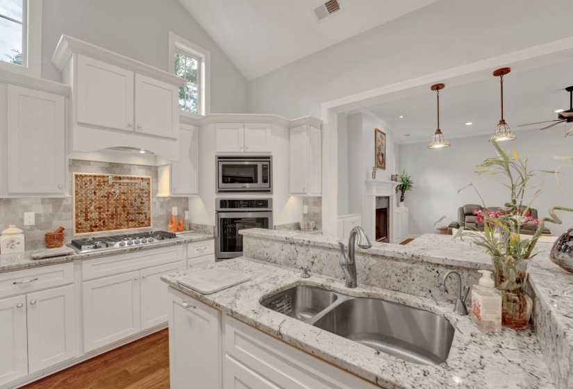 Modern kitchen featuring white cabinetry, light granite countertops, stainless steel appliances, and a gas range with a decorative tile backsplash