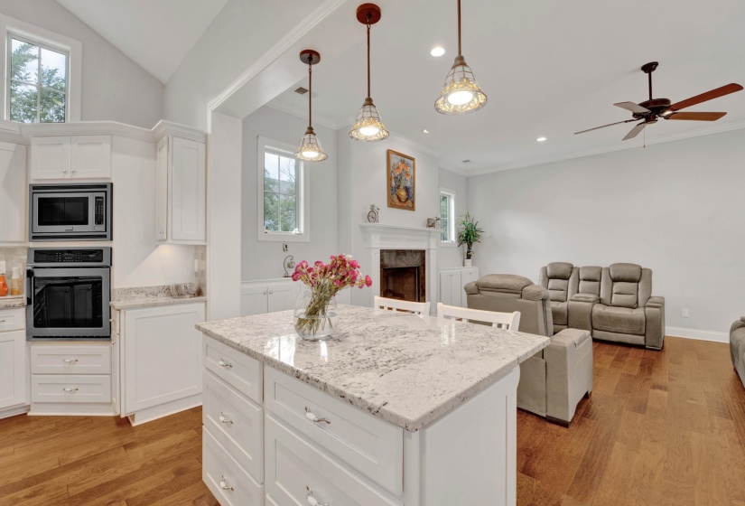 Open-concept living area featuring a kitchen island with stone countertop, white cabinetry, integrated oven and microwave, recessed lighting, and wood-finish flooring