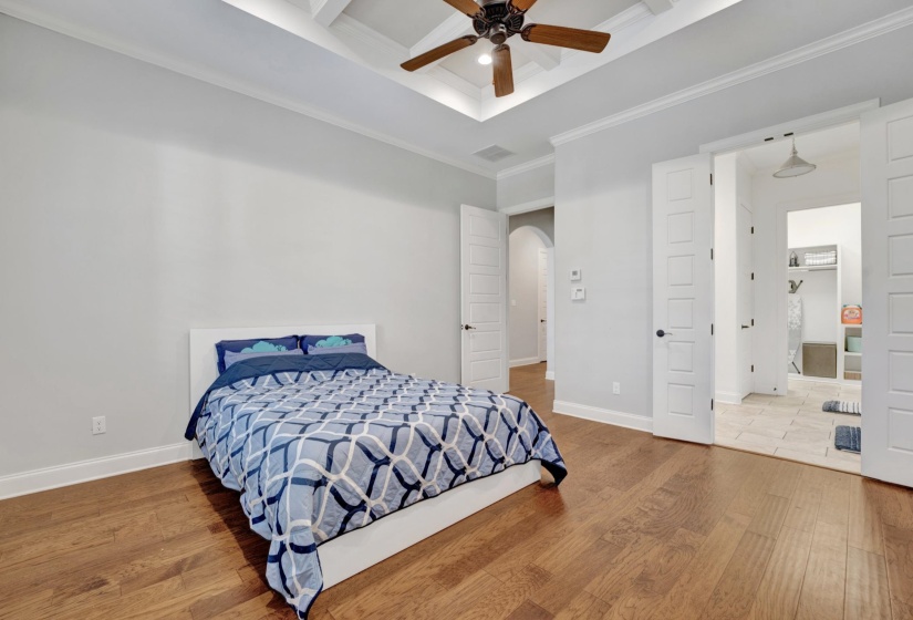 Spacious room featuring wood-finish flooring, a tray ceiling with a ceiling fan, and white trim molding