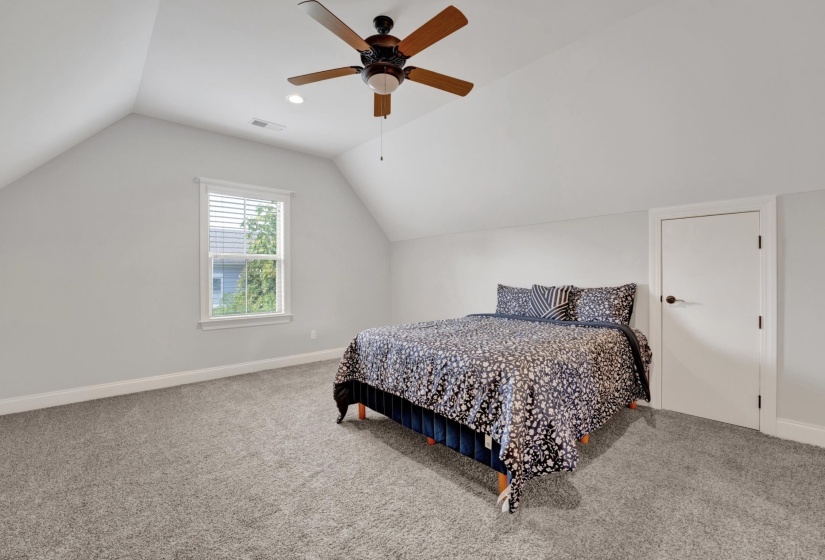 Carpeted room featuring an angled ceiling, a window with horizontal blinds, a white door, and a ceiling fan with integrated lighting