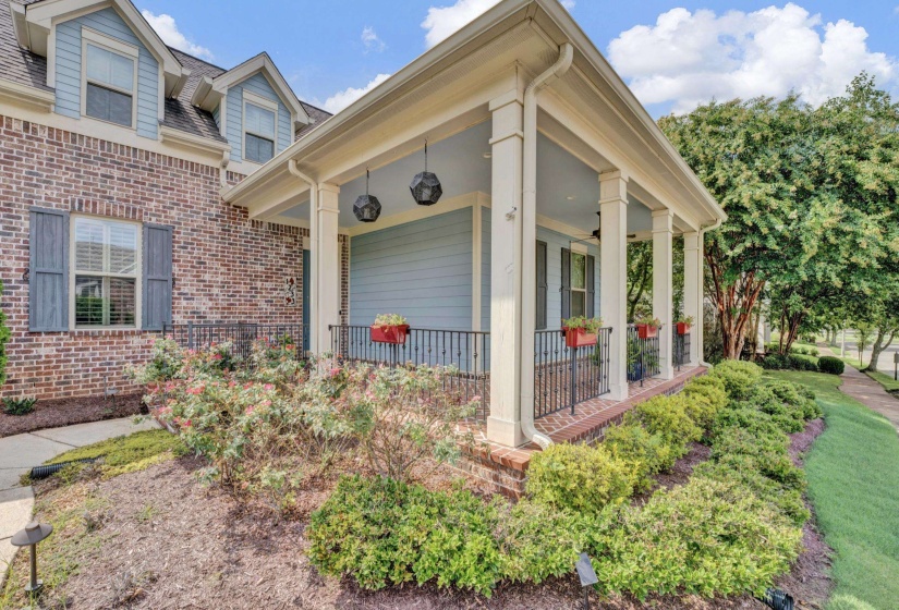 Brick facade home featuring a covered front porch with substantial columns, wrought iron railing, and hanging pendant lights