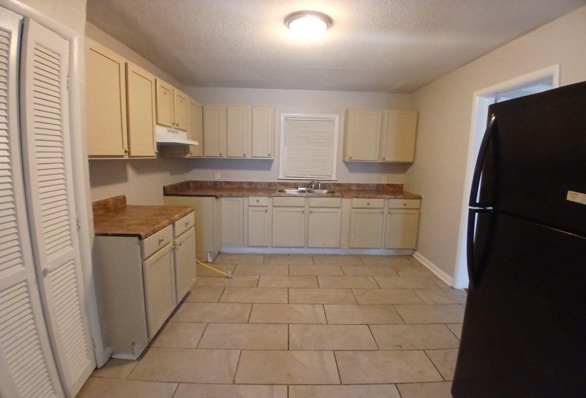 Kitchen featuring extensive cream cabinetry, light-toned tile flooring, and a window with blinds