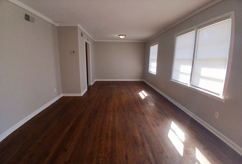 Spacious room featuring wood-finish flooring, light grey painted walls, white crown molding, and multiple windows with blinds