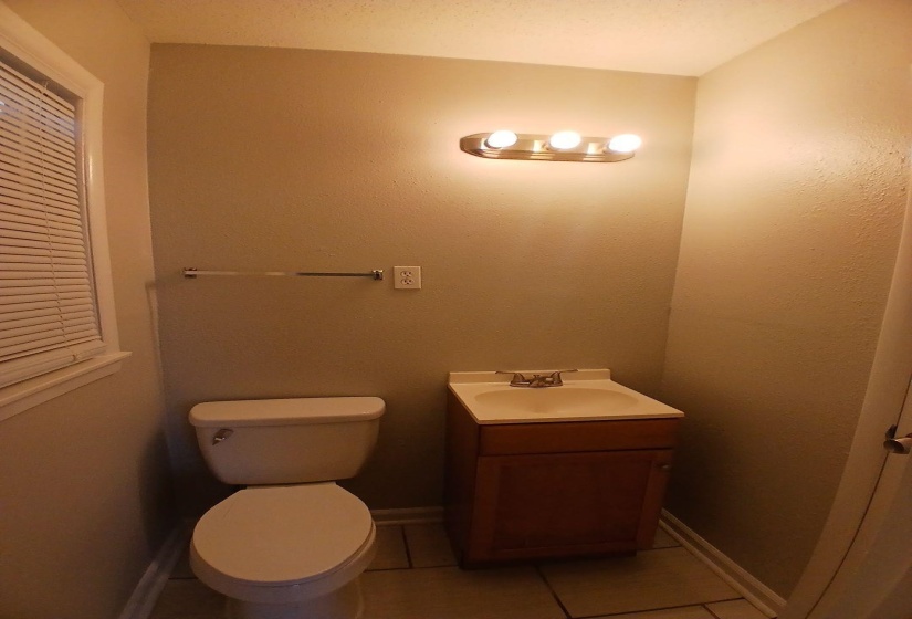 Compact bathroom featuring a single window with blinds, a toilet, and a vanity with an integrated sink