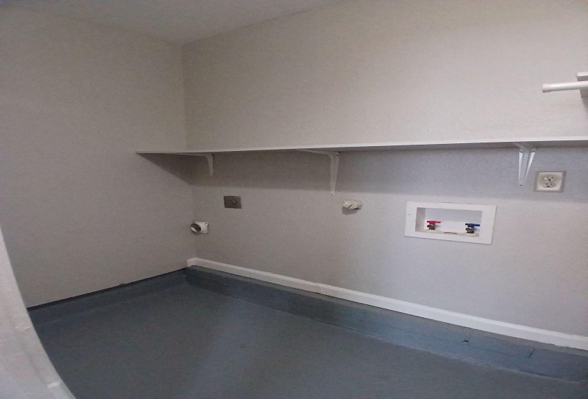 Dedicated laundry area featuring a utility sink connection, electrical outlet, and an overhead storage shelf