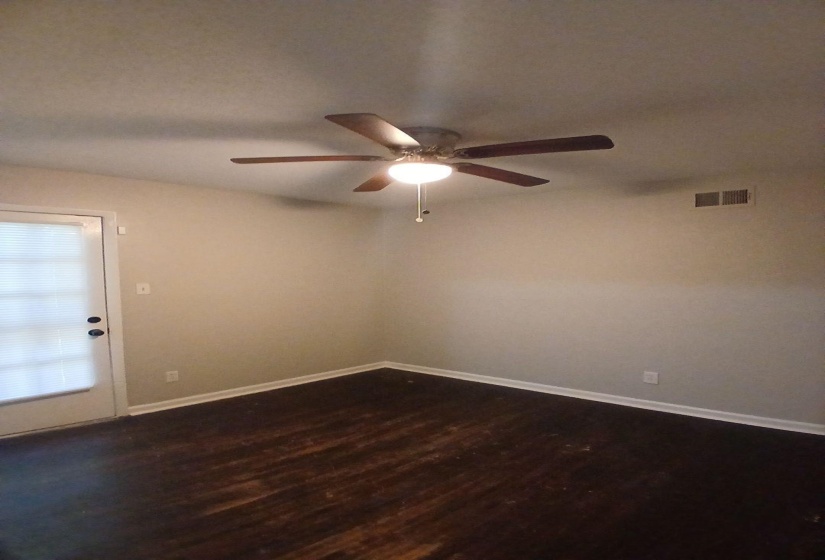 Room featuring a ceiling fan with integrated lighting, dark wood-finish flooring, light-toned walls, white baseboards, and a glass-paneled door