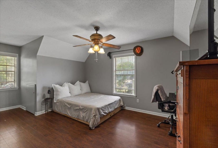 Spacious room featuring wood-finish flooring, a ceiling fan with integrated lighting, and multiple windows with blinds
