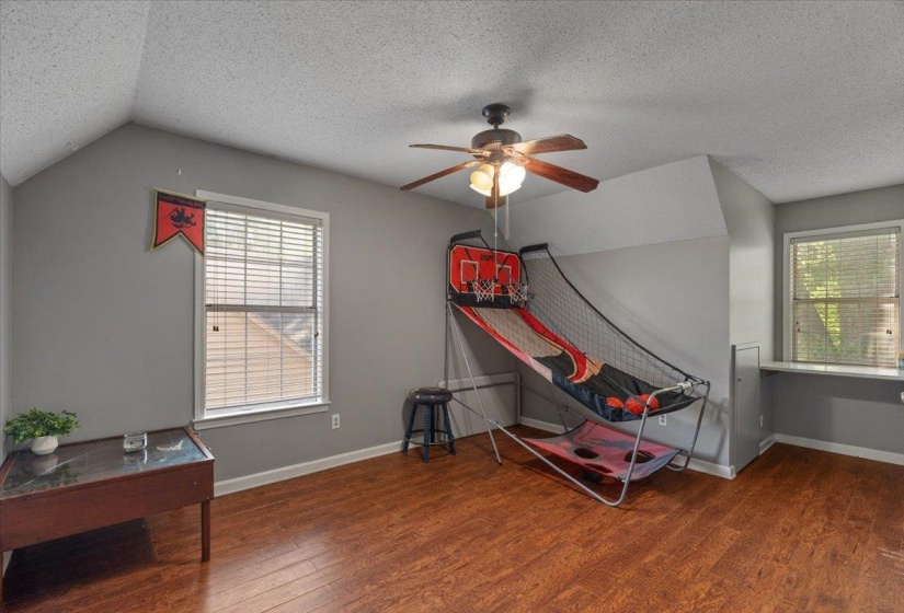 Spacious room featuring rich wood-finish flooring, a ceiling fan, and multiple windows with blinds
