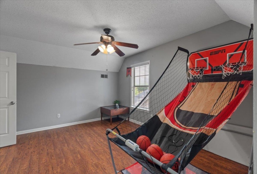 Spacious room featuring wood-finish flooring, neutral gray walls, a ceiling fan with integrated lighting, and natural light from a window with blinds