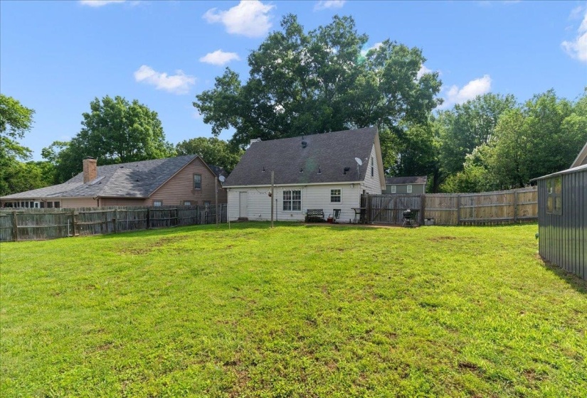 Expansive grassy backyard featuring a white siding exterior, dark shingle roof, and a privacy fence