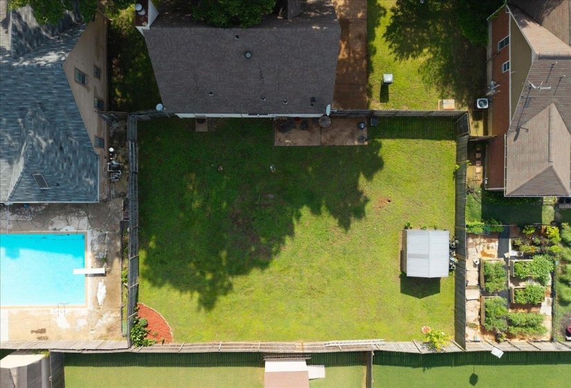 Expansive, enclosed backyard featuring a large green lawn, perimeter fencing, and a storage shed