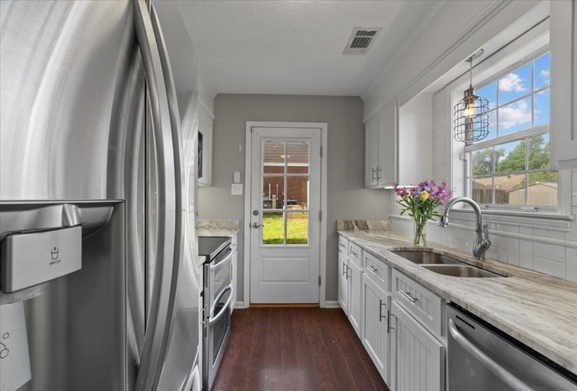 Galley kitchen featuring stainless steel appliances, white cabinetry, and wood-finish flooring