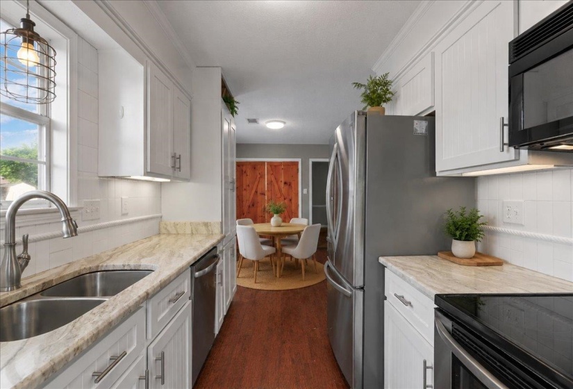 Galley kitchen featuring white cabinetry, light-toned countertops, a stainless steel double basin sink, and a full suite of stainless steel appliances