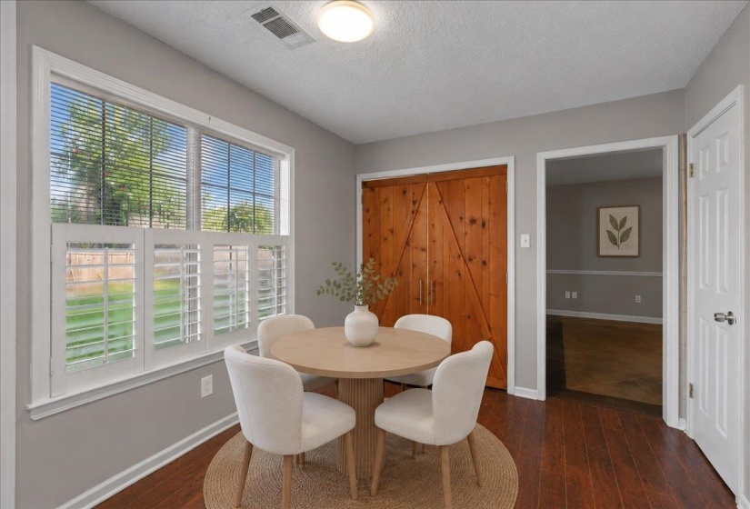 Dining area featuring wood-finish flooring, a large window with white plantation shutters, and a natural wood barn door