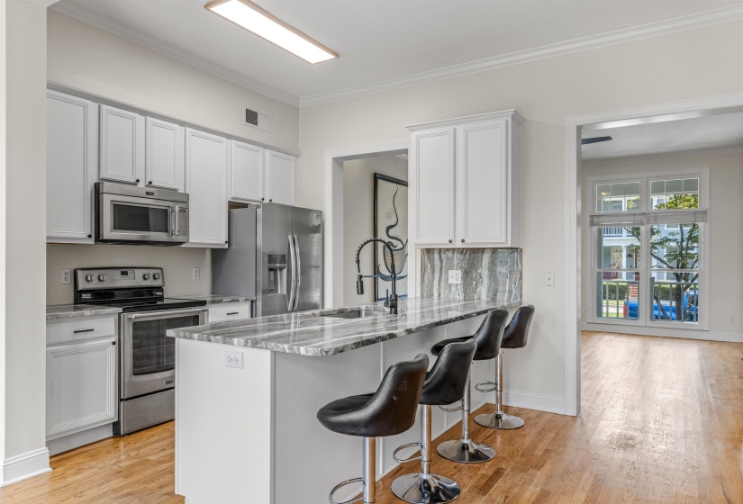 Kitchen featuring white shaker-style cabinetry, stainless steel appliances, a large island with an integrated breakfast bar, and wood-finish flooring
