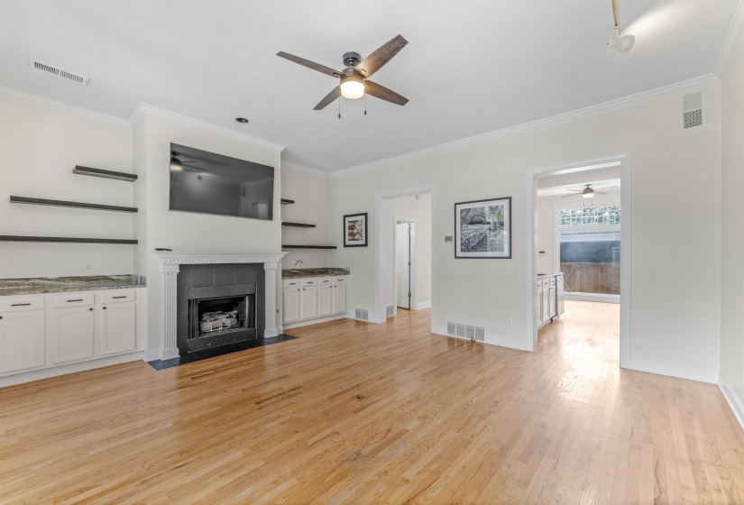 Expansive living space featuring hardwood flooring, a fireplace with a mantel, built-in cabinetry with stone countertops, open shelving, and crown molding