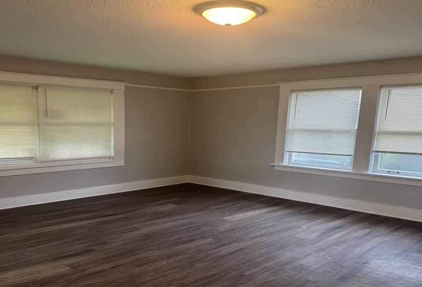 Room featuring wood-finish flooring, two window units with blinds, and neutral wall paint