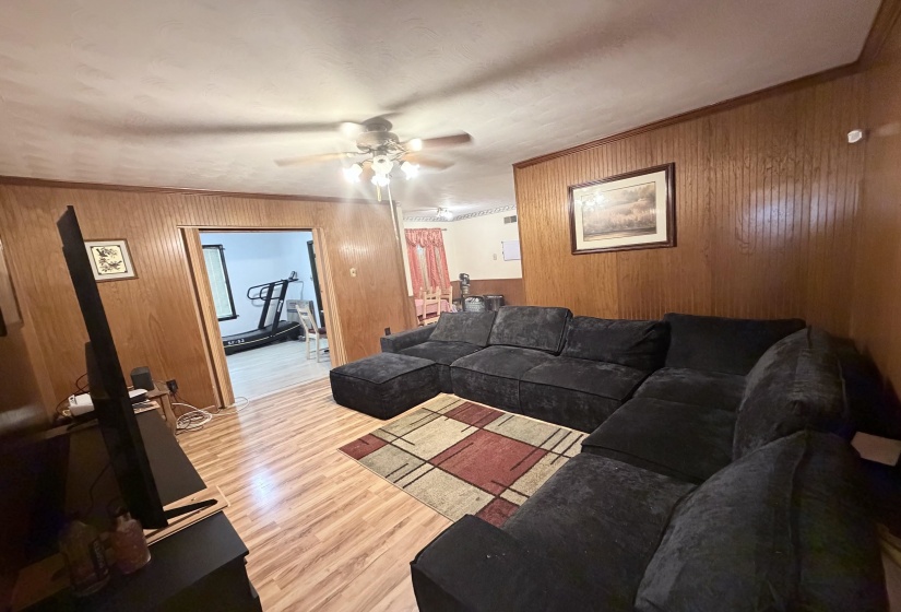 Living area featuring wood-finish flooring, wood paneling, and a ceiling fan with integrated lighting