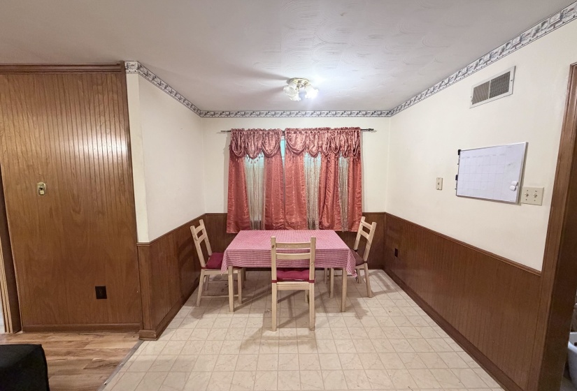 Dining area featuring wood-finish paneling, patterned wallpaper border, and neutral tile flooring