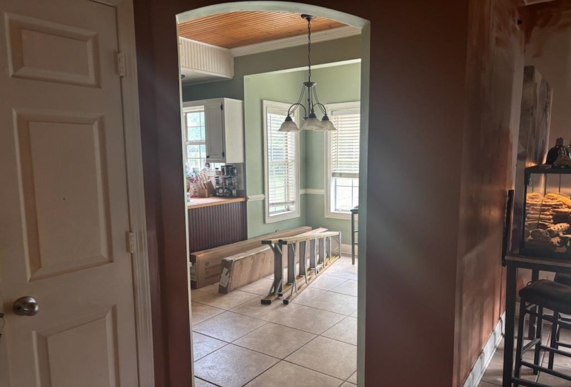 Archway entry with a coffered wood-finish ceiling, tile flooring, two windows with blinds, and a multi-light chandelier