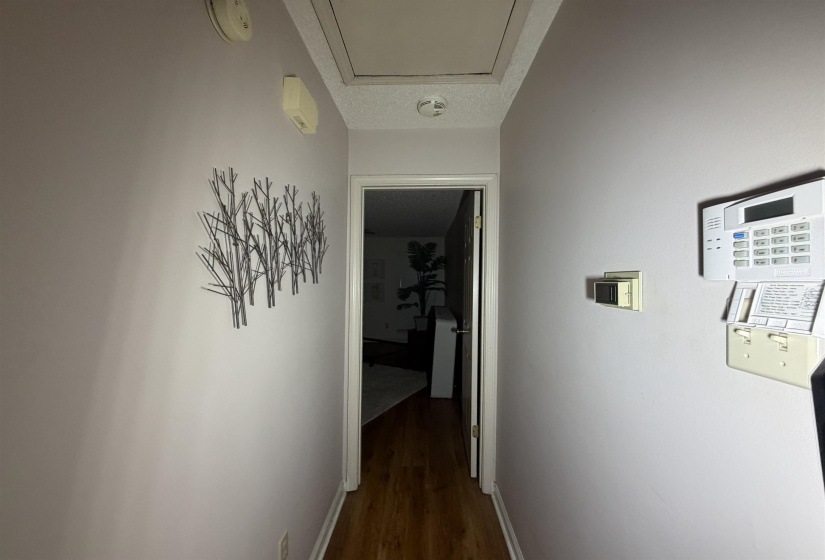 Hallway featuring wood-finish flooring, light-toned walls, and an overhead access panel