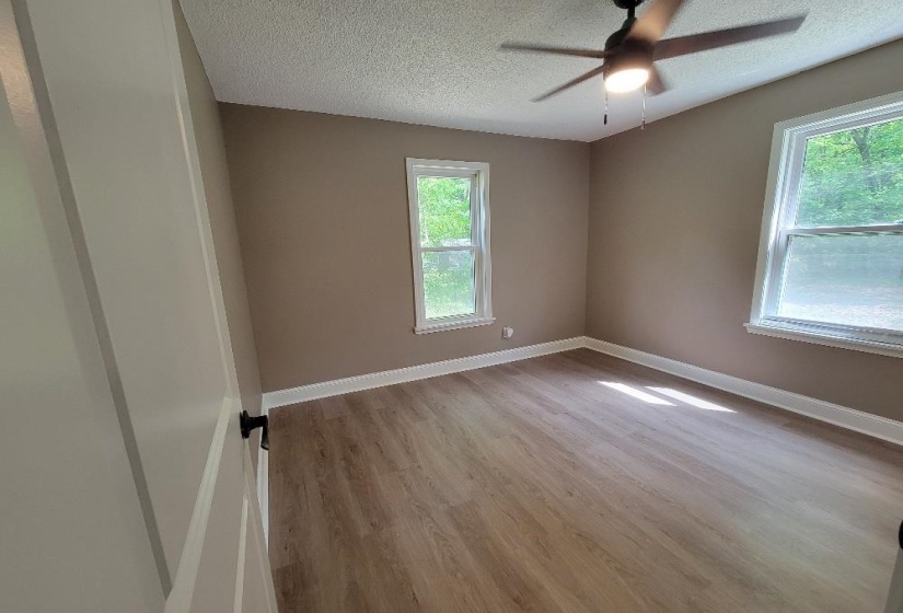Spacious room featuring light wood-finish flooring, neutral wall paint, white trim, and a ceiling fan with integrated lighting