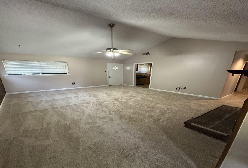 Unfurnished living room with a ceiling fan, carpet floors, a textured ceiling, baseboards, and vaulted ceiling