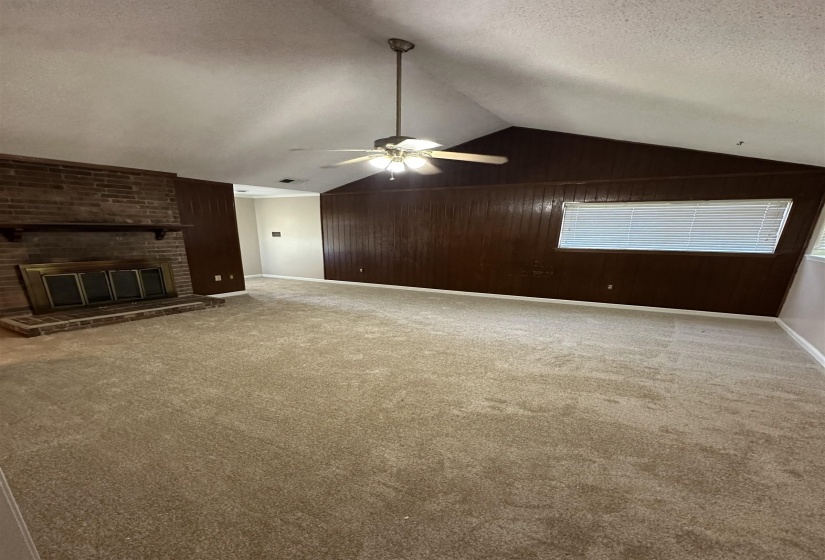 Unfurnished living room featuring vaulted ceiling, wooden walls, a brick fireplace, a textured ceiling, and carpet floors