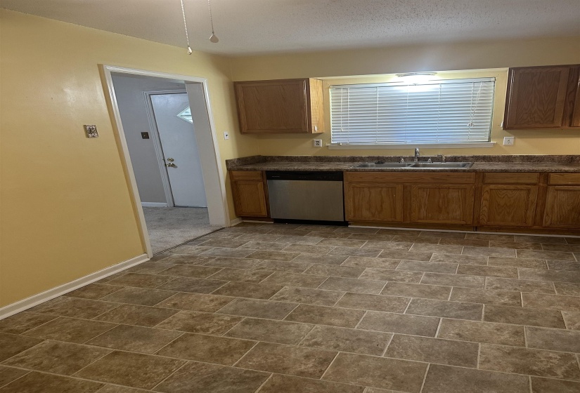 Kitchen with a sink, dishwasher, dark countertops, baseboards, and brown cabinets