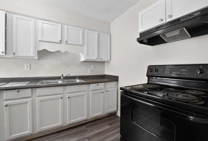 Kitchen featuring black / electric stove, white cabinetry, exhaust hood, dark countertops, and a textured ceiling
