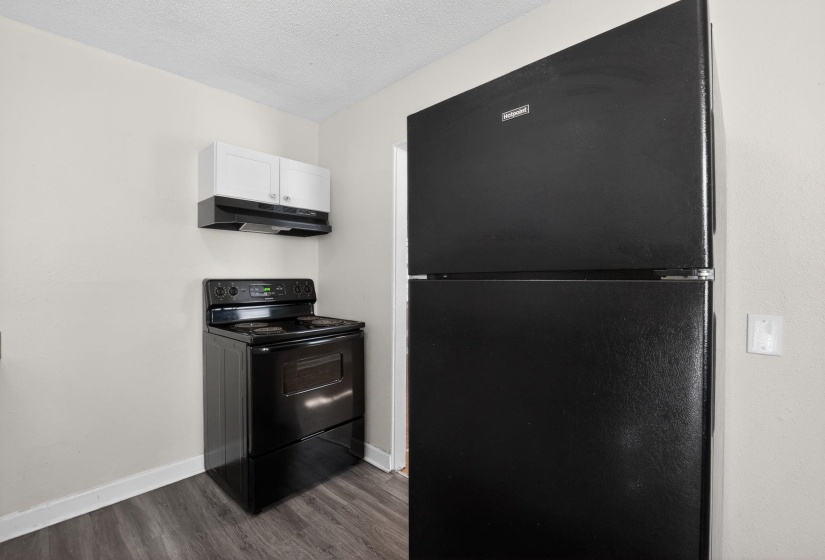 Kitchen featuring black appliances, under cabinet range hood, a textured ceiling, dark wood-style floors, and white cabinetry