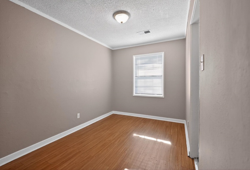Empty room featuring a textured ceiling, light wood-type flooring, crown molding, and a textured wall