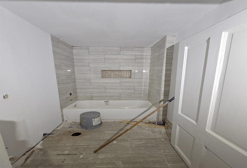 New bathtub installation with grey horizontal tile surround and integrated mosaic niche