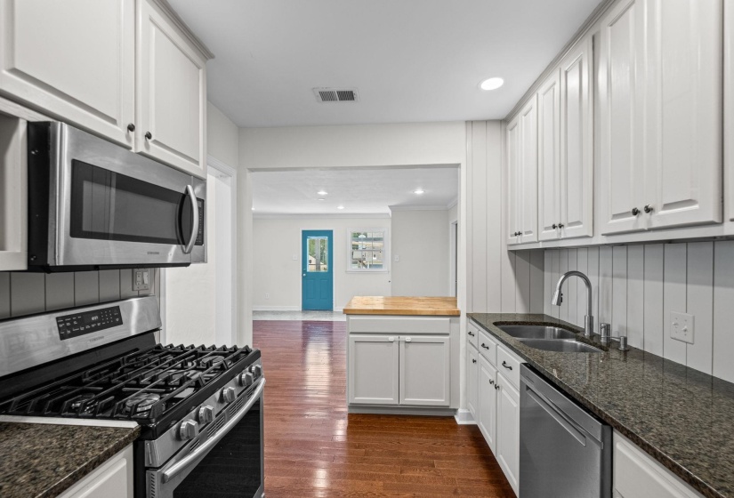 Kitchen featuring white shaker cabinetry, stainless steel appliances, dark stone countertops, and wood-finish flooring