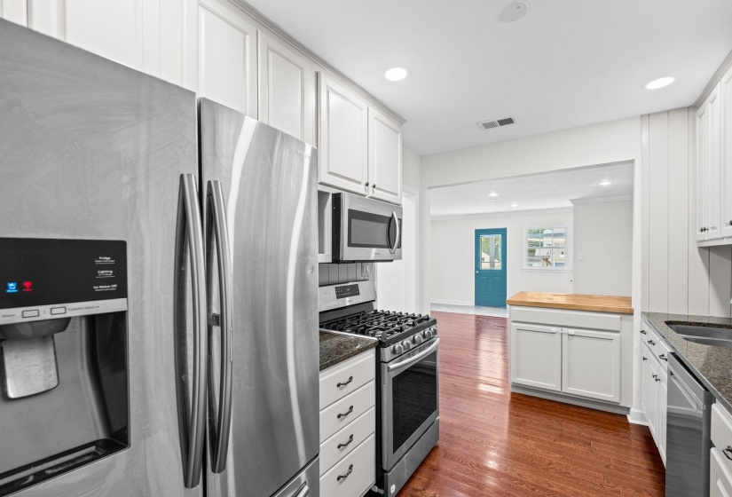 Kitchen featuring stainless steel appliances, white cabinetry, dark stone countertops, wood-finish flooring, and recessed lighting
