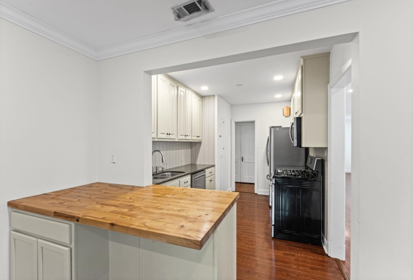 Kitchen featuring a wood-finish countertop island, cream cabinetry, stainless steel appliances, and wood-finish flooring