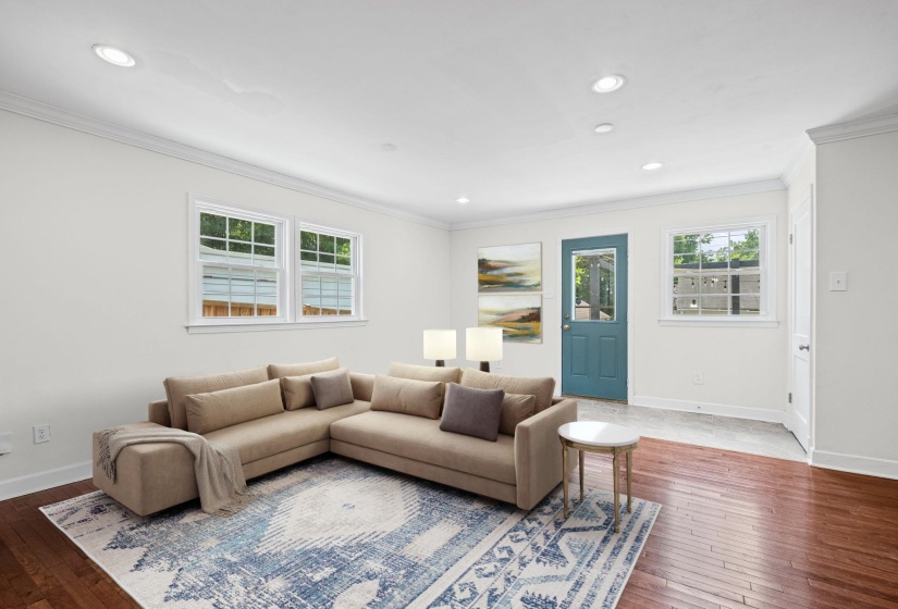 Open living area featuring recessed lighting, crown molding, wood-finish flooring, multiple windows, and a vibrant teal door