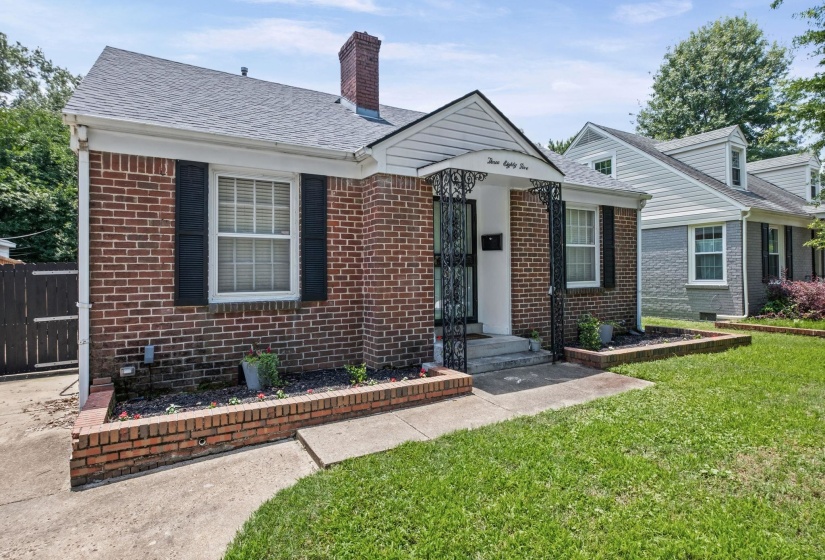 Brick exterior with dark shutters, a covered front entry with wrought iron accents, and a sidewalk leading to the front door